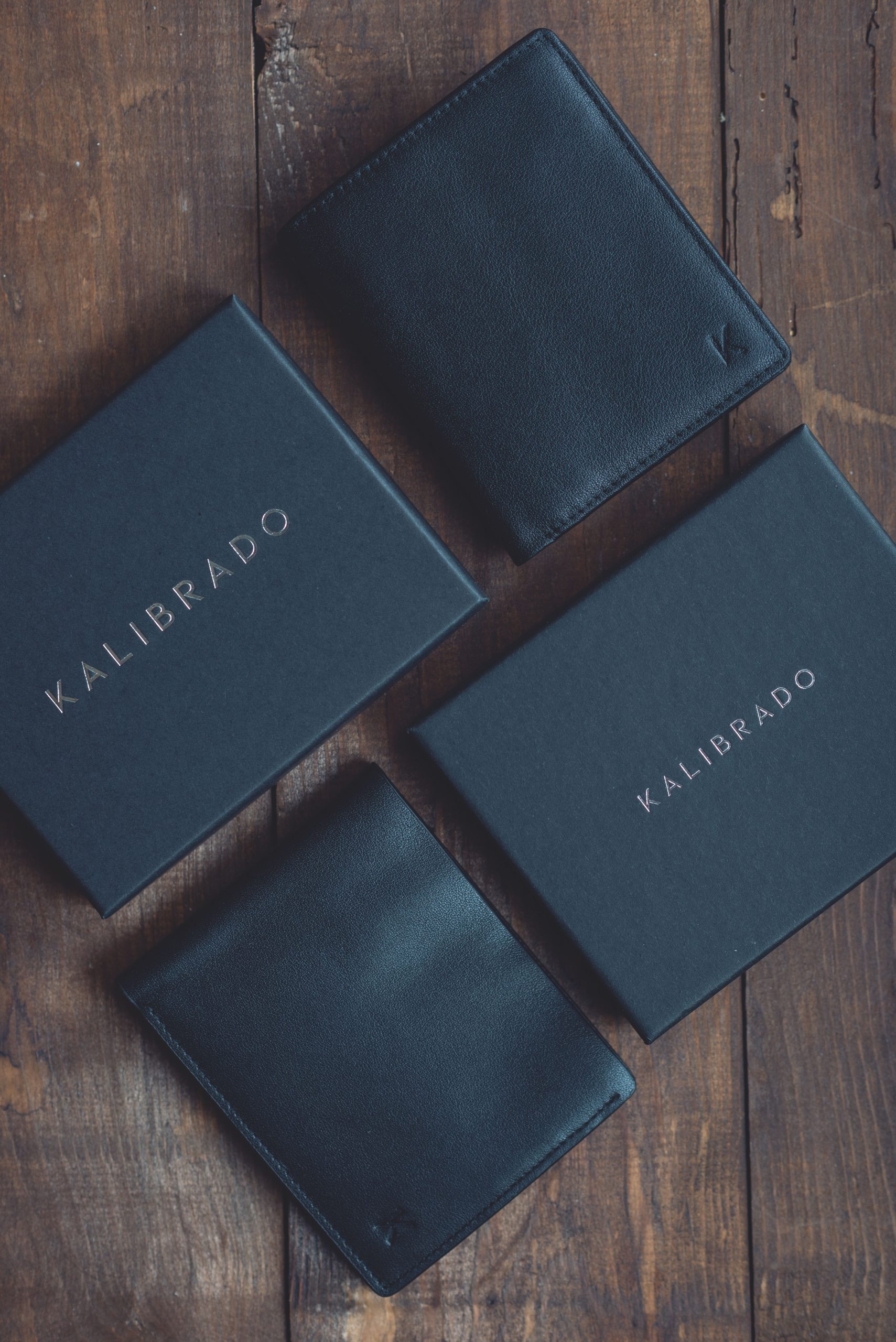 A premium full-grain leather wallet, notebook and accessories displayed on a dark wooden desk, highlighting the natural grain and rich texture of quality leather.