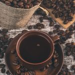 A beautifully styled cup of freshly brewed coffee beside whole Arabica and Robusta beans on a dark wooden table, highlighting the contrast between the world's two most popular coffee varieties.
