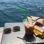 A premium pair of polarised sunglasses resting on a wooden table overlooking a bright coastal landscape, illustrating the difference in glare reduction and visual clarity.