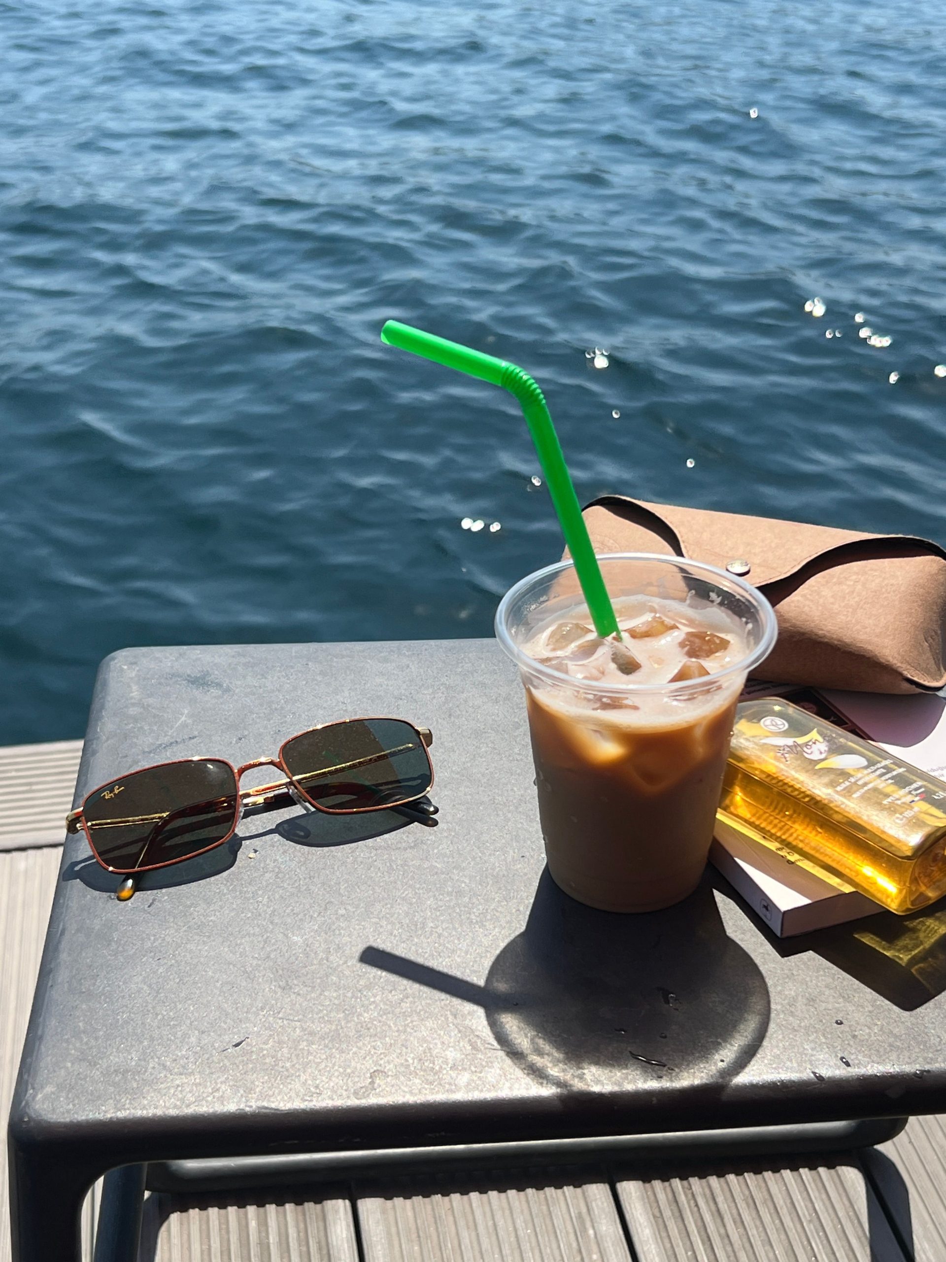 A premium pair of polarised sunglasses resting on a wooden table overlooking a bright coastal landscape, illustrating the difference in glare reduction and visual clarity.